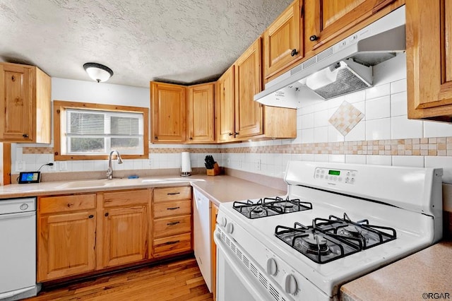 kitchen with tasteful backsplash, sink, light wood-type flooring, white appliances, and a textured ceiling