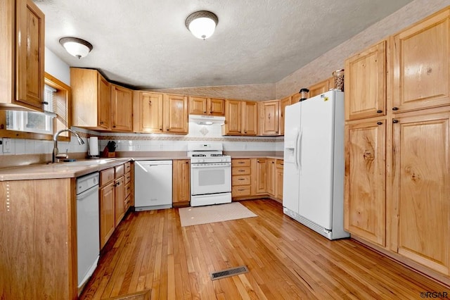 kitchen featuring light brown cabinetry, sink, vaulted ceiling, light hardwood / wood-style flooring, and white appliances