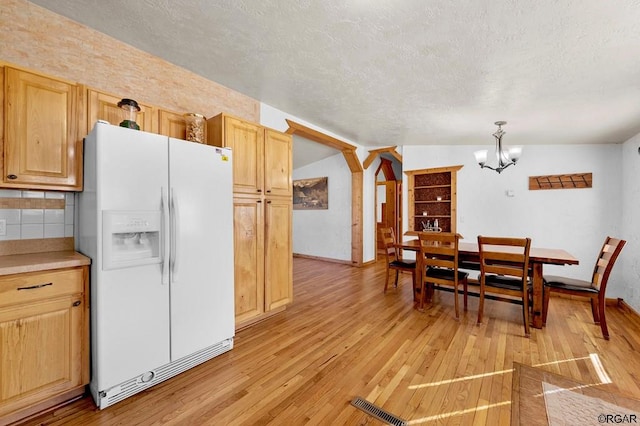 dining area with light hardwood / wood-style flooring, a notable chandelier, vaulted ceiling, and a textured ceiling