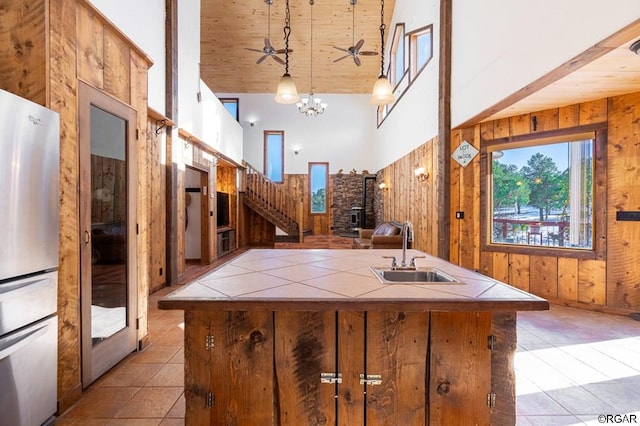 kitchen featuring sink, wood walls, decorative light fixtures, refrigerator, and high vaulted ceiling