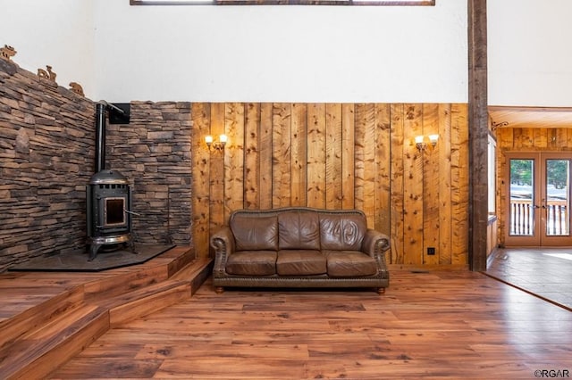 living area with wood-type flooring, a wood stove, wood walls, and french doors