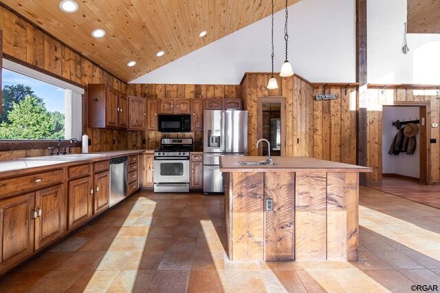 kitchen featuring an island with sink, appliances with stainless steel finishes, wooden walls, and high vaulted ceiling