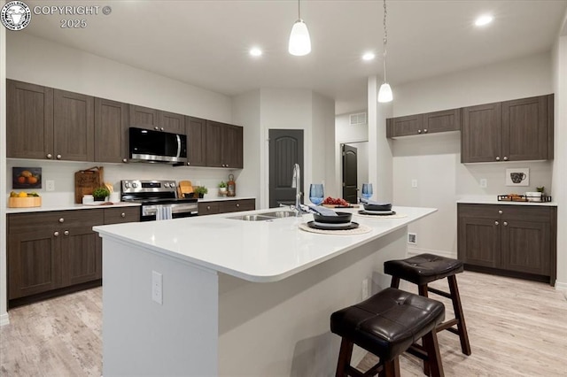 kitchen with a breakfast bar, an island with sink, sink, light hardwood / wood-style floors, and stainless steel appliances