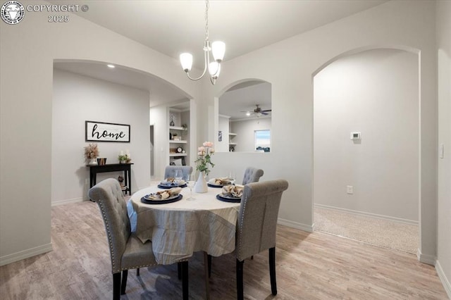 dining space with built in shelves, ceiling fan with notable chandelier, and light hardwood / wood-style flooring