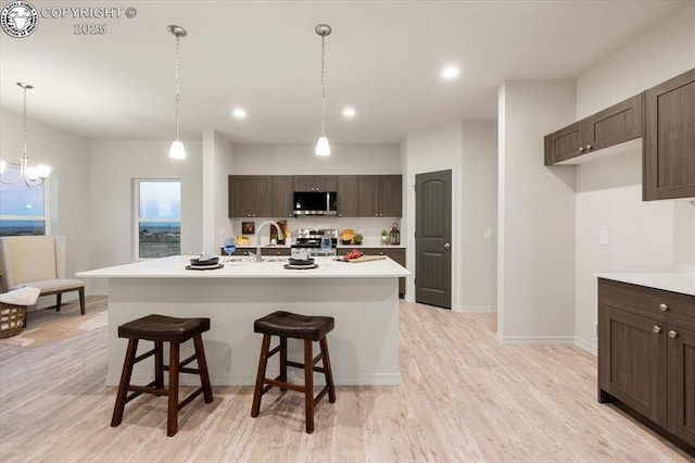 kitchen featuring dark brown cabinetry, appliances with stainless steel finishes, a center island with sink, and a kitchen bar