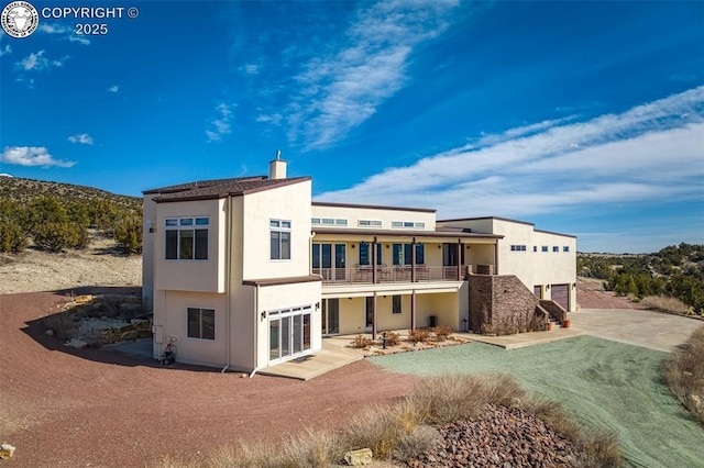 rear view of property with a balcony, a chimney, and stucco siding