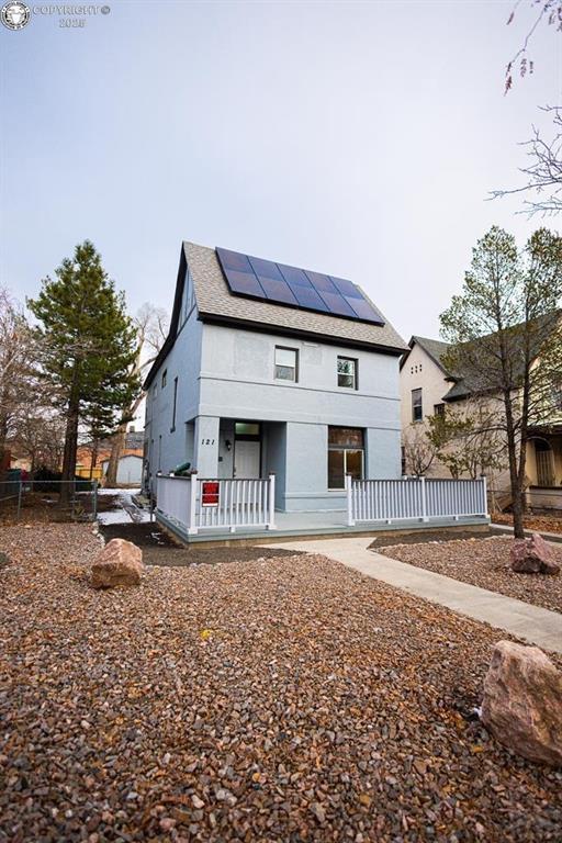 121 W Evans Ave, Pueblo, CO 81004 - view of front of house with covered porch, fence, stucco siding, solar panels, and a shingled roof