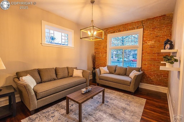121 W Evans Ave, Pueblo, CO 81004 - living room featuring a notable chandelier, brick wall, baseboards, and dark wood-style floors