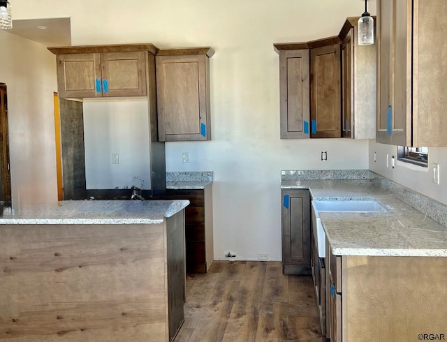 kitchen featuring hanging light fixtures, light stone countertops, sink, and dark hardwood / wood-style flooring