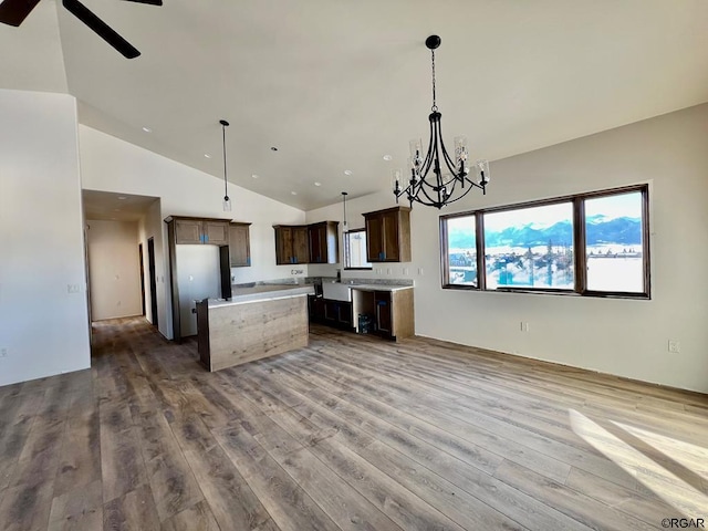 kitchen featuring decorative light fixtures, high vaulted ceiling, light hardwood / wood-style floors, a kitchen island, and ceiling fan with notable chandelier