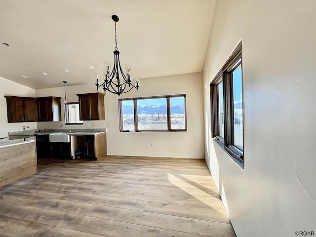 kitchen with lofted ceiling, dark brown cabinetry, light hardwood / wood-style floors, decorative light fixtures, and a chandelier