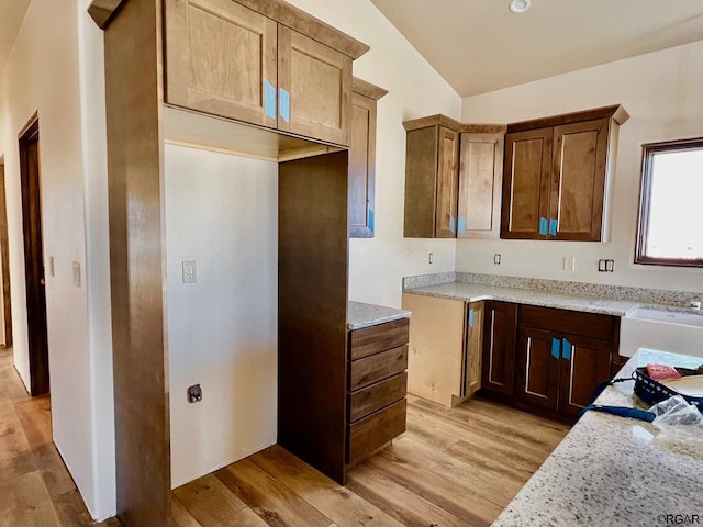 kitchen featuring light stone countertops, lofted ceiling, sink, and light hardwood / wood-style flooring