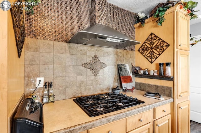 kitchen featuring tasteful backsplash, black gas cooktop, light brown cabinets, and wall chimney range hood