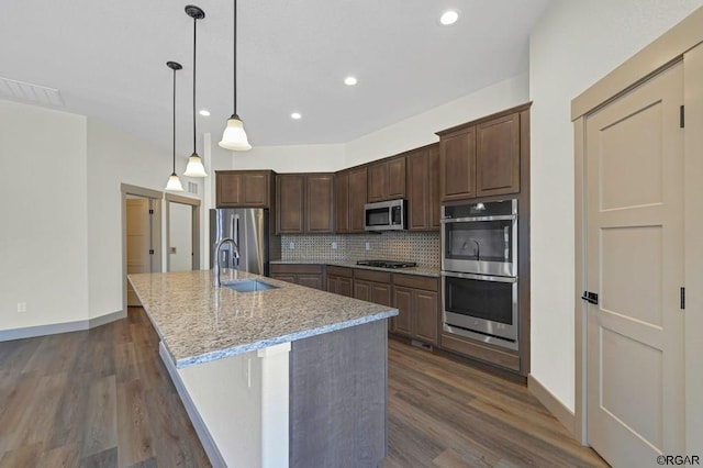 kitchen featuring sink, light stone counters, decorative light fixtures, a center island with sink, and appliances with stainless steel finishes