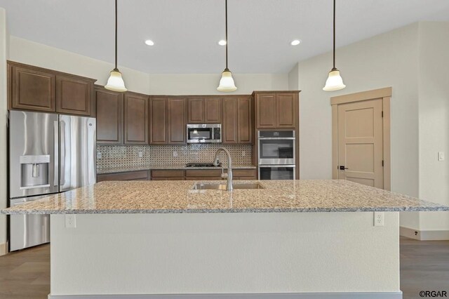 kitchen with stainless steel appliances, an island with sink, sink, and light stone counters