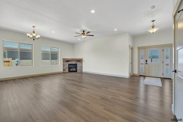 unfurnished living room featuring hardwood / wood-style flooring, a stone fireplace, and ceiling fan with notable chandelier