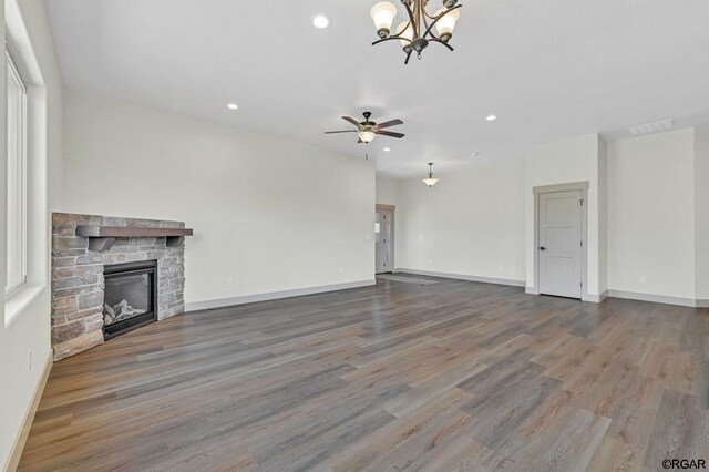 unfurnished living room with hardwood / wood-style flooring, a stone fireplace, and ceiling fan with notable chandelier