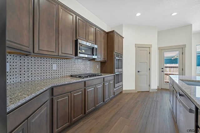 kitchen with dark brown cabinetry, stainless steel appliances, light stone countertops, and wood-type flooring