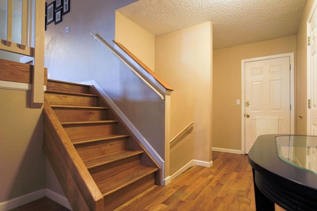 stairs with hardwood / wood-style floors and a textured ceiling