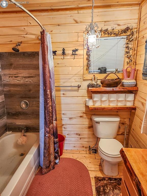 297 S Matterhorn Cir, Westcliffe, CO 81252 - full bathroom with wood finished floors, toilet, shower / bathtub combination with curtain, and wood walls
