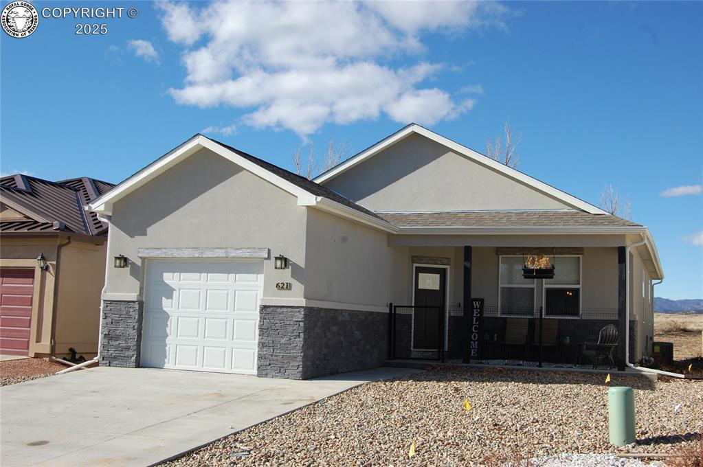 single story home featuring covered porch, stucco siding, stone siding, and a garage
