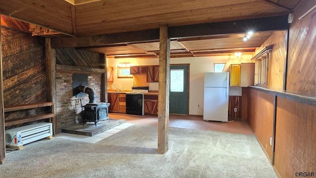 basement with wooden walls, white refrigerator, light carpet, wooden ceiling, and a wood stove