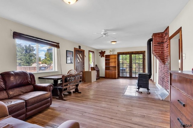 living room with plenty of natural light, light hardwood / wood-style floors, ceiling fan, and a wood stove