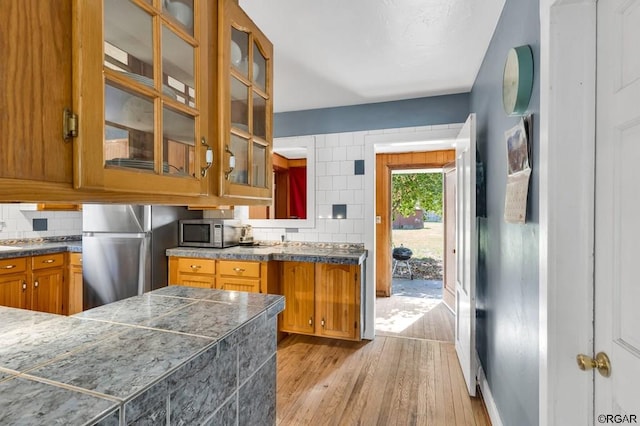 kitchen with fridge, kitchen peninsula, light hardwood / wood-style flooring, and backsplash