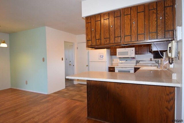 kitchen with dark wood-type flooring, white appliances, kitchen peninsula, and sink