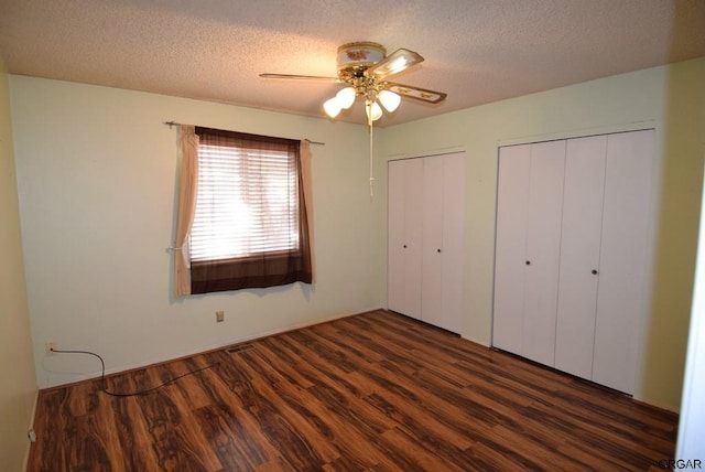 unfurnished bedroom with dark hardwood / wood-style flooring, a textured ceiling, ceiling fan, and two closets