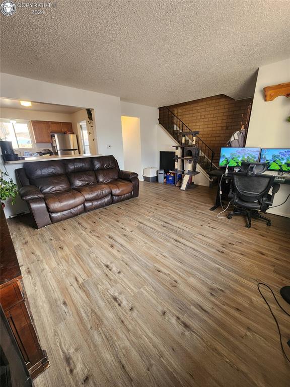 living room with brick wall, a textured ceiling, and light hardwood / wood-style floors