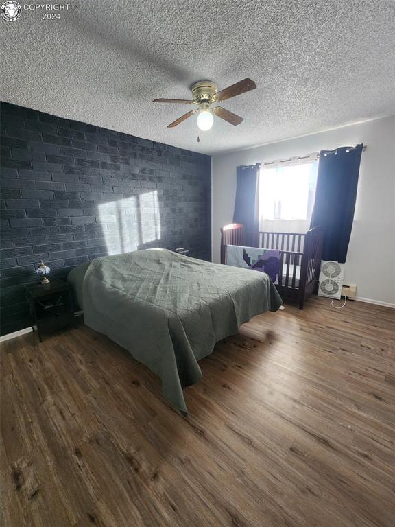 bedroom featuring brick wall, dark wood-type flooring, a textured ceiling, and ceiling fan