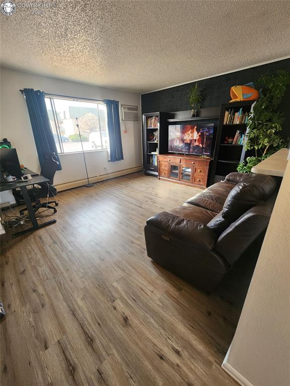 living room featuring a baseboard heating unit, wood-type flooring, a wall mounted AC, and a textured ceiling