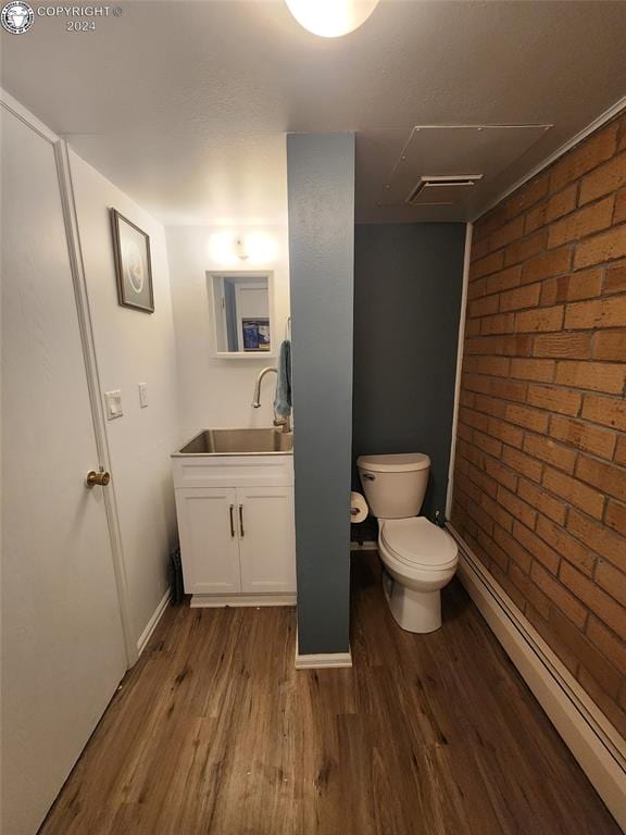 bathroom with brick wall, wood-type flooring, toilet, and vanity