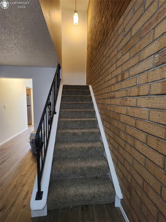 stairs featuring brick wall, hardwood / wood-style floors, and a textured ceiling