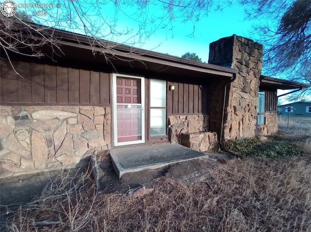 entrance to property featuring board and batten siding, stone siding, and a chimney