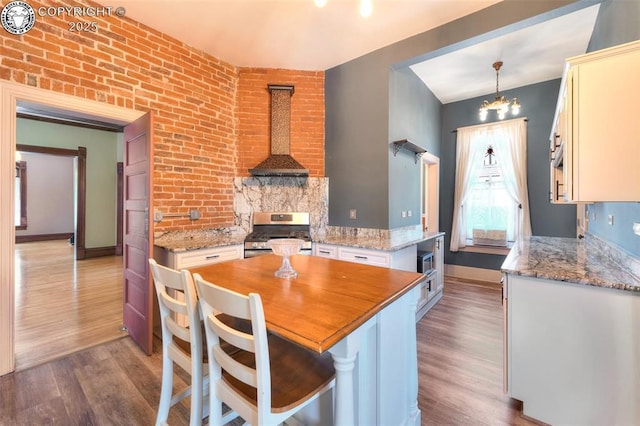 417 Greenwood Ave, Canon City, CO 81212 - kitchen with stainless steel gas range oven, wall chimney exhaust hood, wood finished floors, a chandelier, and light stone counters