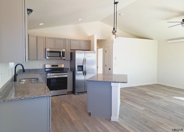 kitchen with sink, light stone counters, appliances with stainless steel finishes, a kitchen island, and pendant lighting