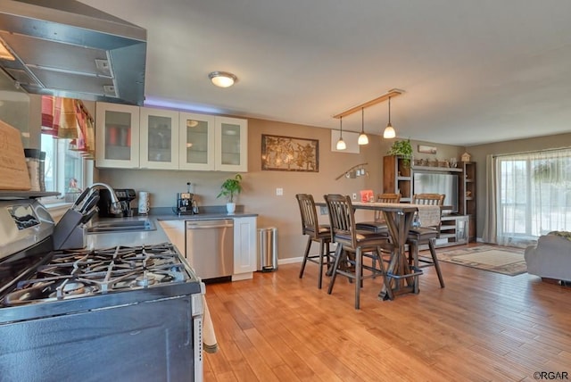 kitchen with sink, exhaust hood, hanging light fixtures, stainless steel appliances, and white cabinets