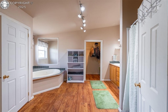 full bath with track lighting, a walk in closet, vanity, wood finished floors, and a bath