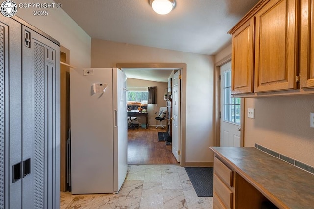 interior space with freestanding refrigerator, dark countertops, brown cabinetry, and lofted ceiling