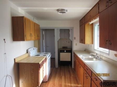 kitchen featuring electric stove, light wood-style flooring, brown cabinets, light countertops, and a sink