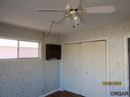 unfurnished bedroom with a ceiling fan, baseboards, a closet, dark wood finished floors, and wallpapered walls