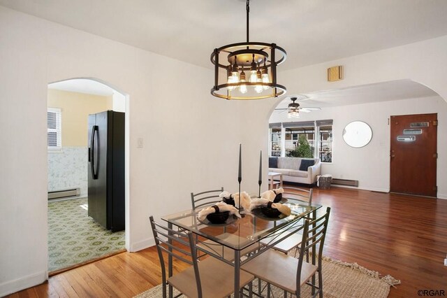 dining area with ceiling fan with notable chandelier, a baseboard radiator, and hardwood / wood-style floors