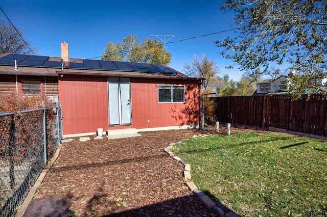 rear view of property with a lawn, an outdoor structure, and solar panels