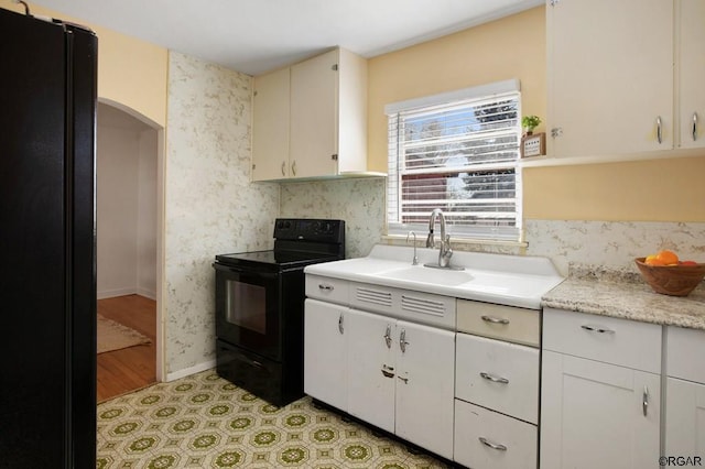 kitchen with sink, white cabinets, light wood-type flooring, and black appliances