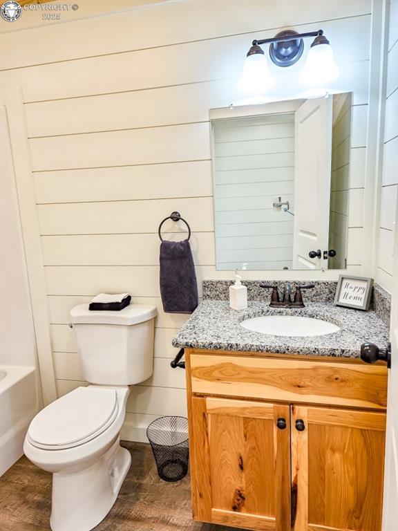 bathroom with toilet, a bathtub, wood finished floors, and vanity