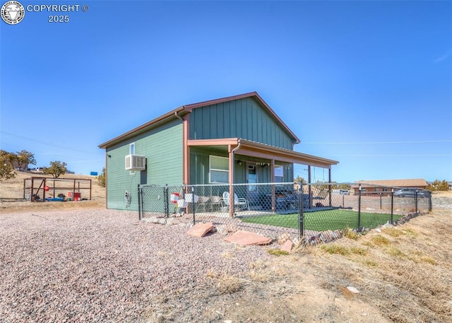 view of front of home with board and batten siding, a front yard, fence, and a wall mounted AC