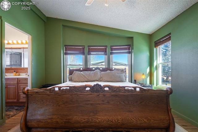 bedroom featuring lofted ceiling, connected bathroom, wood-type flooring, a textured ceiling, and ceiling fan