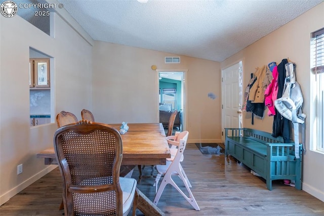 dining space featuring lofted ceiling, hardwood / wood-style floors, and a textured ceiling